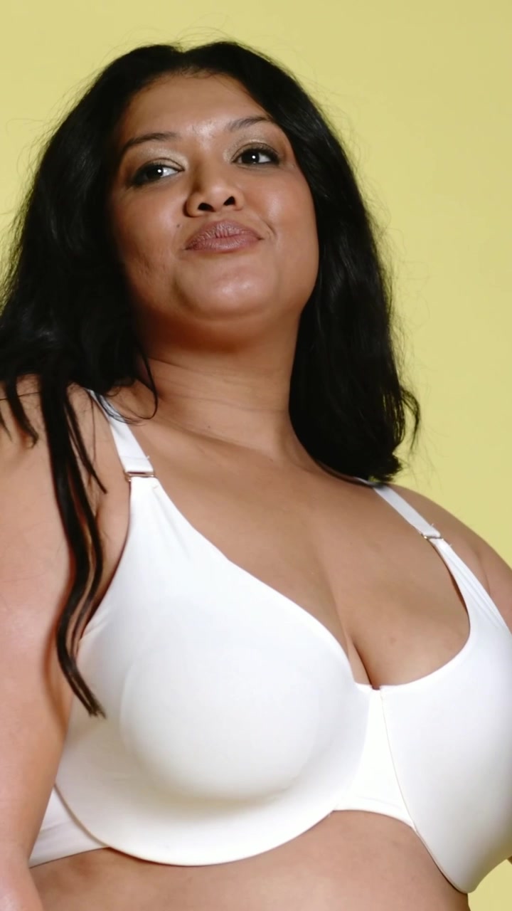 Video verticale: Messa a fuoco sul busto che fa sì che la modella si allunghi e si aggiusti i capelli per la posa in studio, reggiseno bianco.