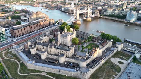 Aerial pan of the Tower of London and Tower Bridge on a warm summer evening, capturing golden light, historic landmarks, and the Thames shimmering beneath the skyline