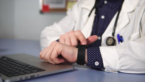 médico comprobando la hora en el reloj inteligente mientras trabaja en la computadora portátil