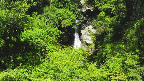 Agua-Blanca-Fresca-Corriendo-Por-La-Ladera-Rocosa-De-La-Cascada-Saltos-Jima-Enclavada-En-Un-Paisaje-De-Follaje-Verde,-Bonao,-República-Dominicana,-Elevación-De-La-Inclinación-Aérea-Hacia-Abajo