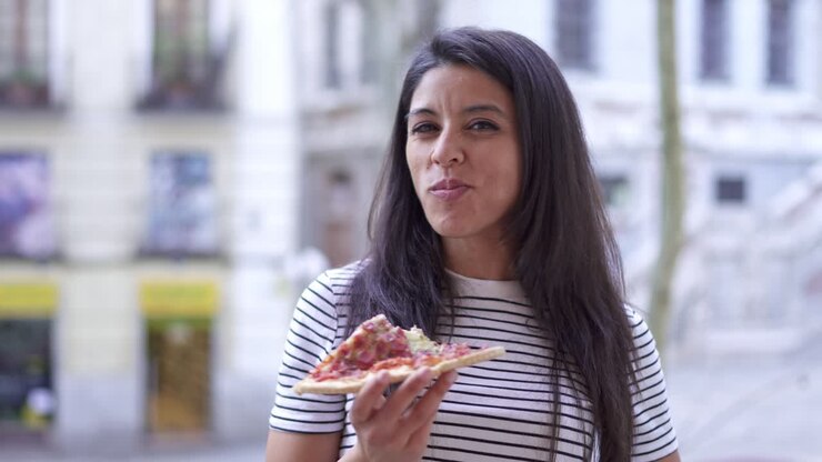 una mujer joven comiendo pizza al aire libre.