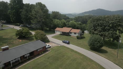 Low-aerial-tracks-automobile-driving-in-green-rural-estate-countryside