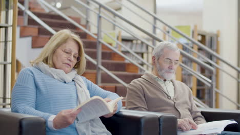 focused senior man and woman sitting in armchairs in library