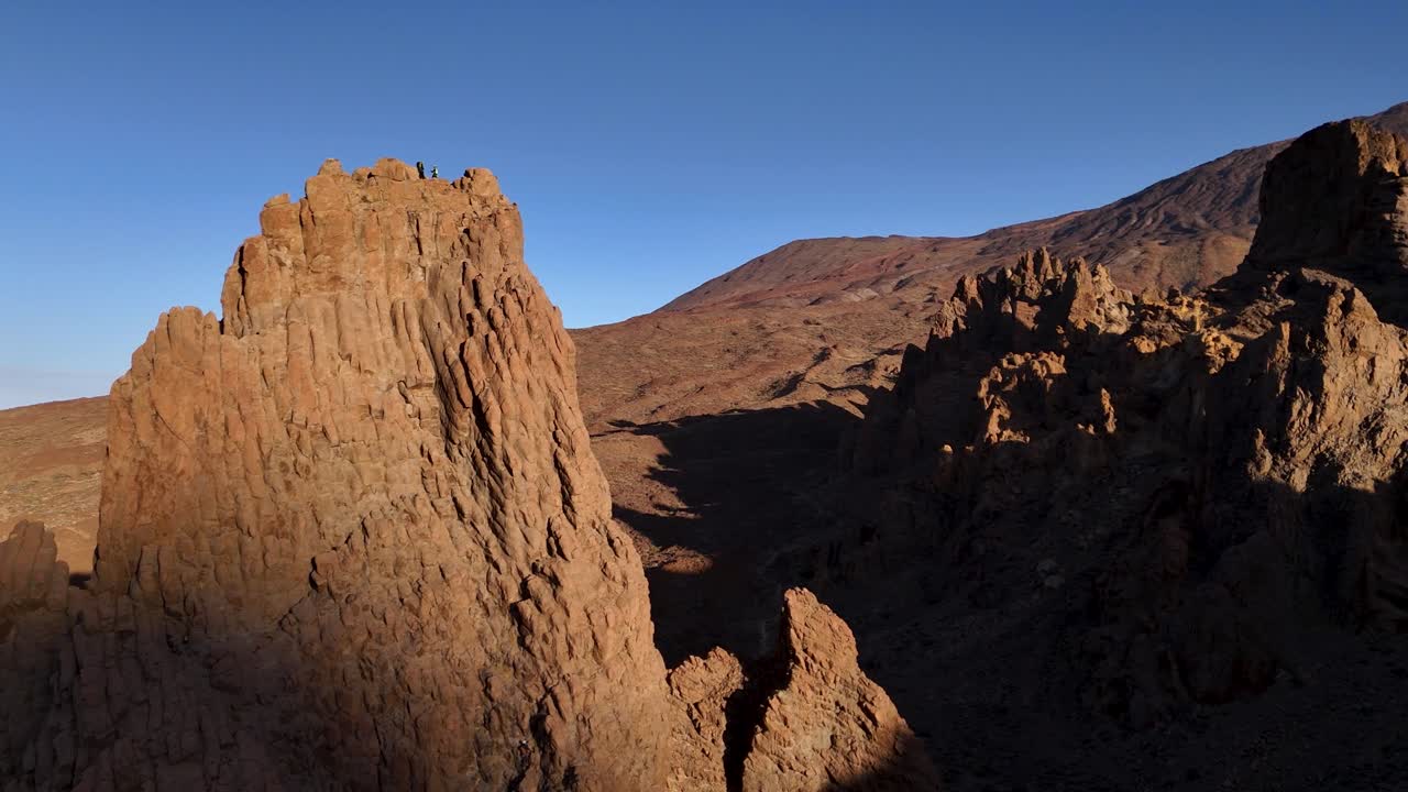 Drone view of rugged mountain peaks under clear blue sky in sunset light
