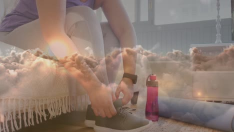 animation of sunset and clouds over woman tying shoe laces, exercising at home