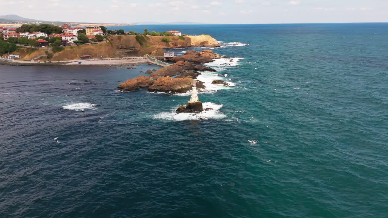 Drone orbits right to left around Ahtopol lighthouse, showing the structure with the mainland and surrounding coastline in the background