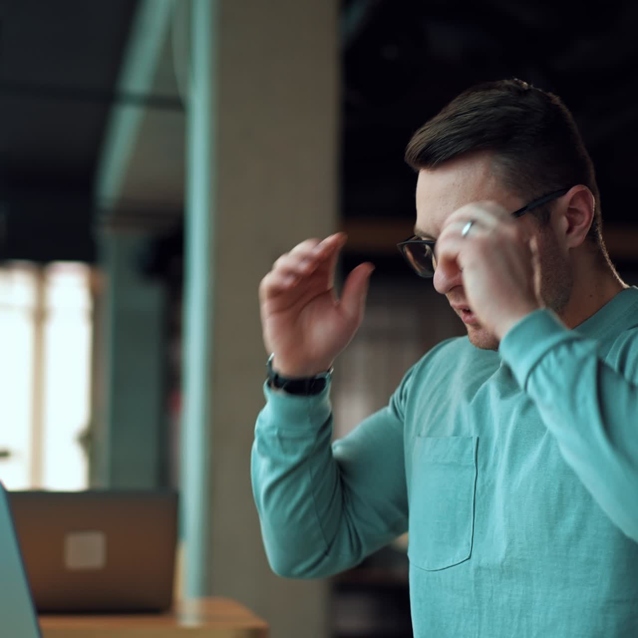 Busy young man working on laptop sitting at desk. Male freelancer closes his gadget, puts off glasses and sits looking straight ahead