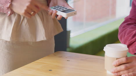 primer plano de un hombre haciendo una compra sin contacto en una cafetería usando una tarjeta de débito o crédito