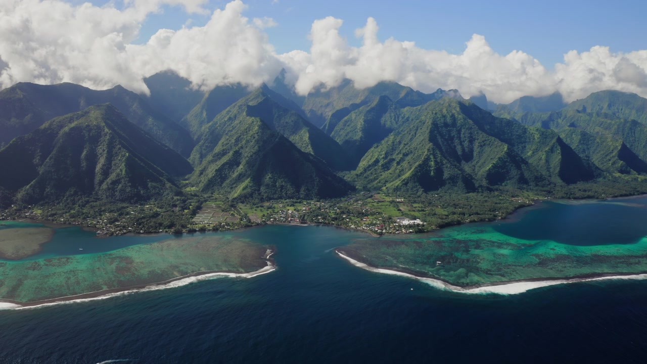 Drone hovers over a Teahupoo valley, Tahiti, dramatic storm clouds rolling above twin reef passes as darker light sweeps across the coastline.
