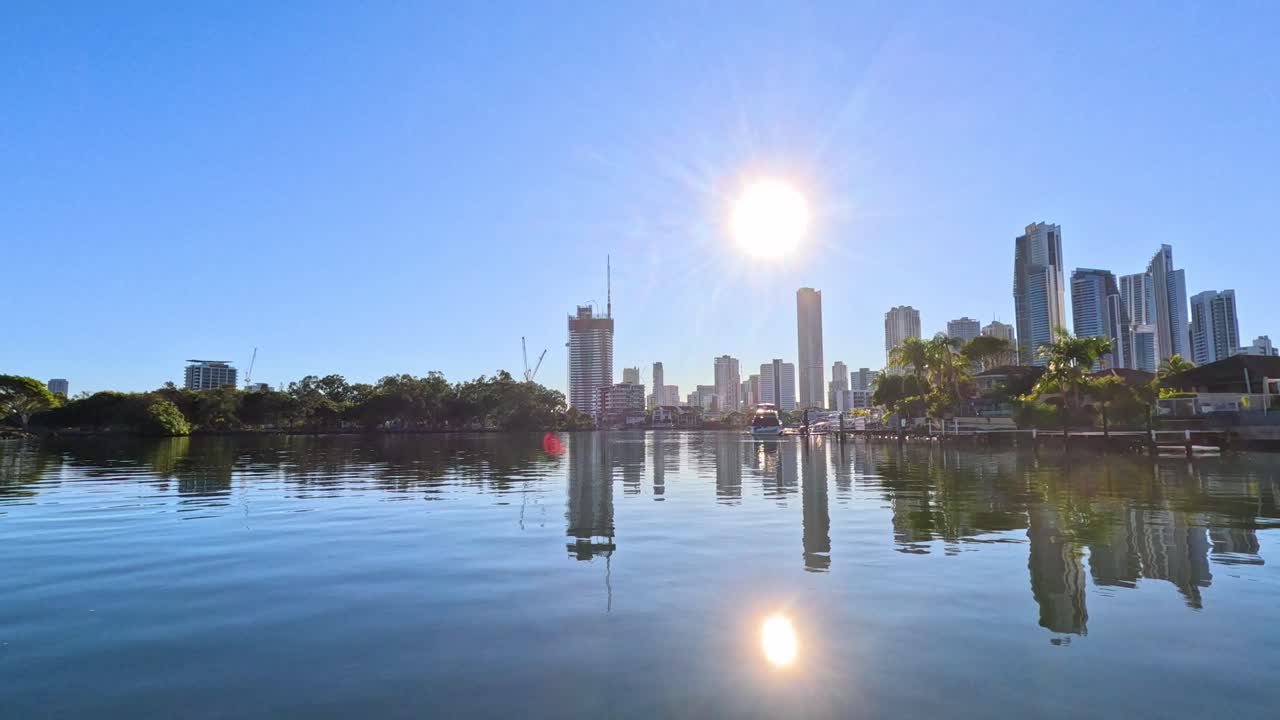 A smooth camera movement glides toward a river speed limit sign with Gold Coast skyscrapers and bright morning sunlight reflecting on calm water