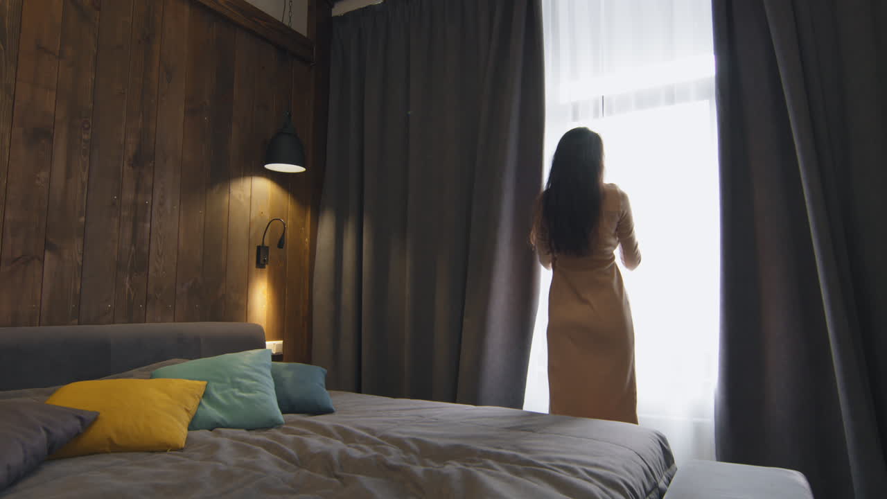 편안한 침실에서 커튼을 열고 있는 여자