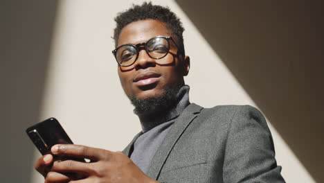 african american businessman using smartphone and smiling at camera