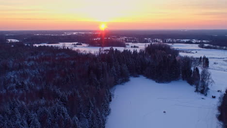 aerial high angle trucking pan of snowy forest and frozen river at sunset, capturing the serene winter landscape, golden flare of red and yellow from sun