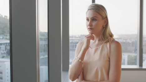 Thoughtful-professional-businesswoman-looking-out-of-a-window-while-her-hand-on-her-chin-in-slow-mot