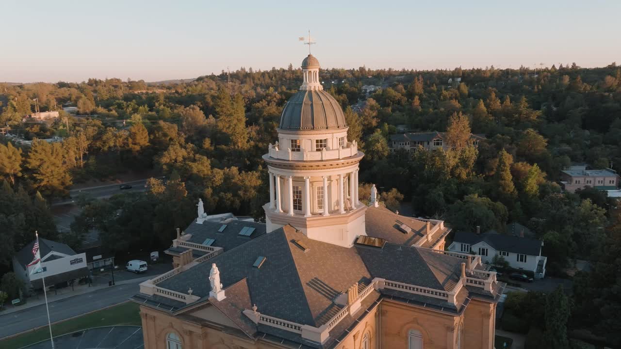 Drone orbiting shot of Auburn Courthouse dome with flags, statues, parking, and trees at golden hour