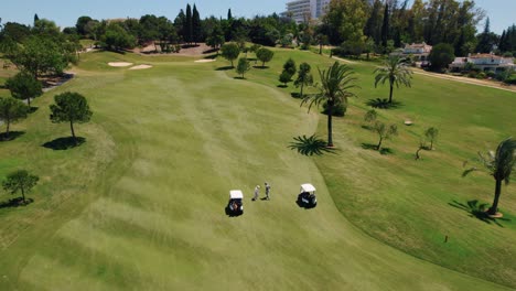 birds eye view of one of the short green lawns of a golf course where two golf carts are parked near golfers