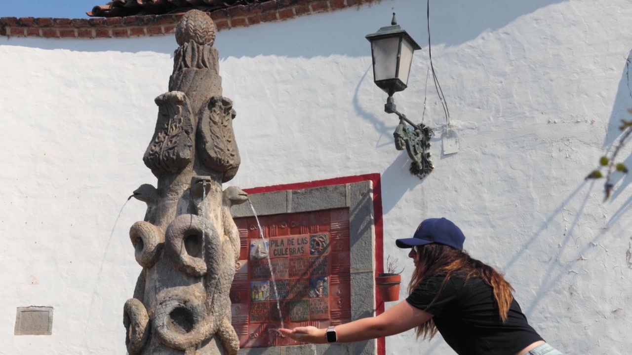 Donna turista che tocca l'acqua che scorre alla fontana del serpente Pila de las Culebras nel centro storico di Tapalpa Pueblo Mágico, Jalisco, Messico. Scatto di viaggio lifestyle
