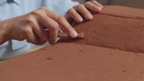 close up of woman automotive designer's hands using rake or wire to create details in the sculpture of car clay in the studio