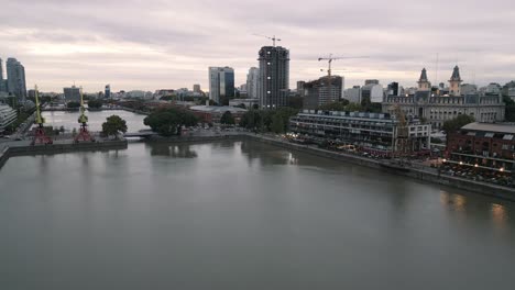 Paisaje-Urbano-Aéreo-De-La-Ciudad-De-Buenos-Aires-Argentina-En-Puerto-Madero,-Microcentro-Durante-La-Puesta-De-Sol-Con-Puerto-Comercial-Y-Grúa