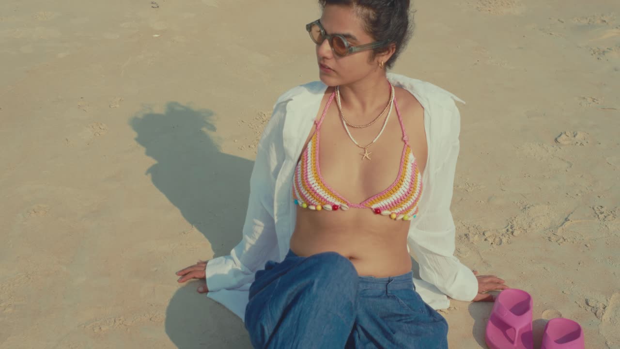 Giovane donna in bikini all'uncinetto seduta su una spiaggia sabbiosa in una scena estiva ventosa