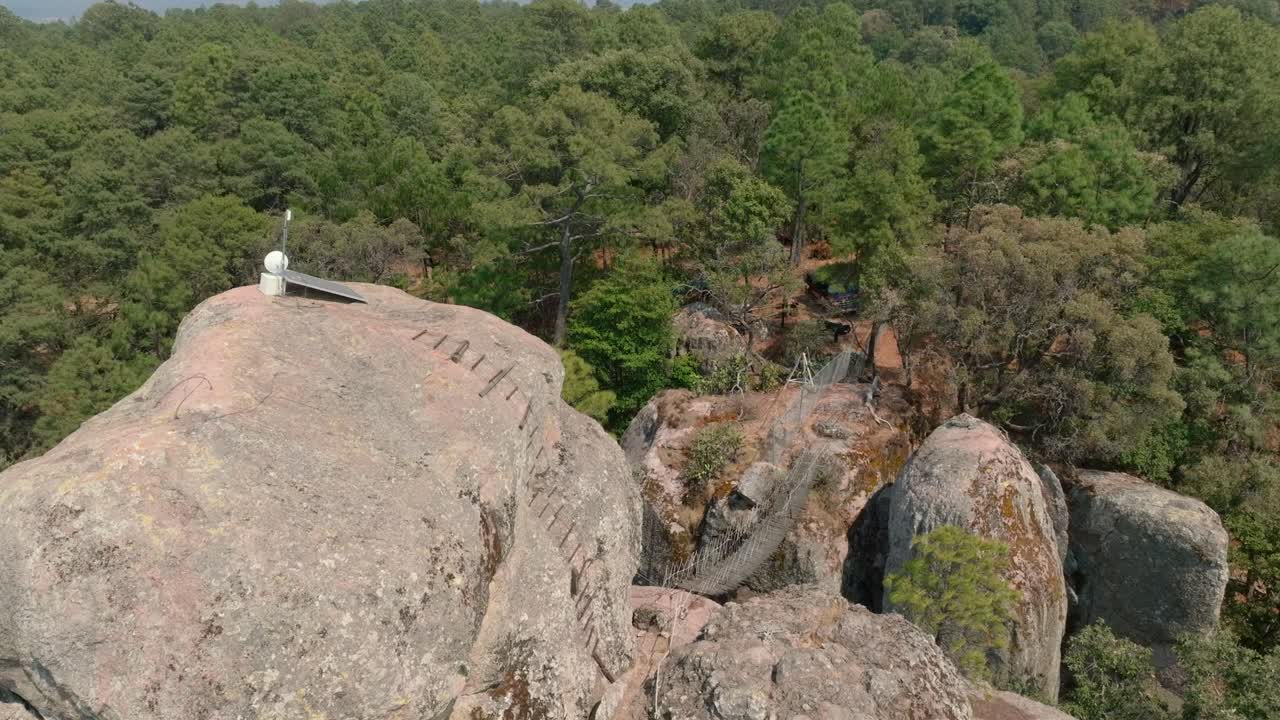 Backward dolly of towering granite monolith with a cross on top, surrounded by dense forest in Tapalpa, Los Frailes Adventure Park, Mexico