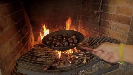 shaking chestnuts as they cook on a pierced pan over the fire