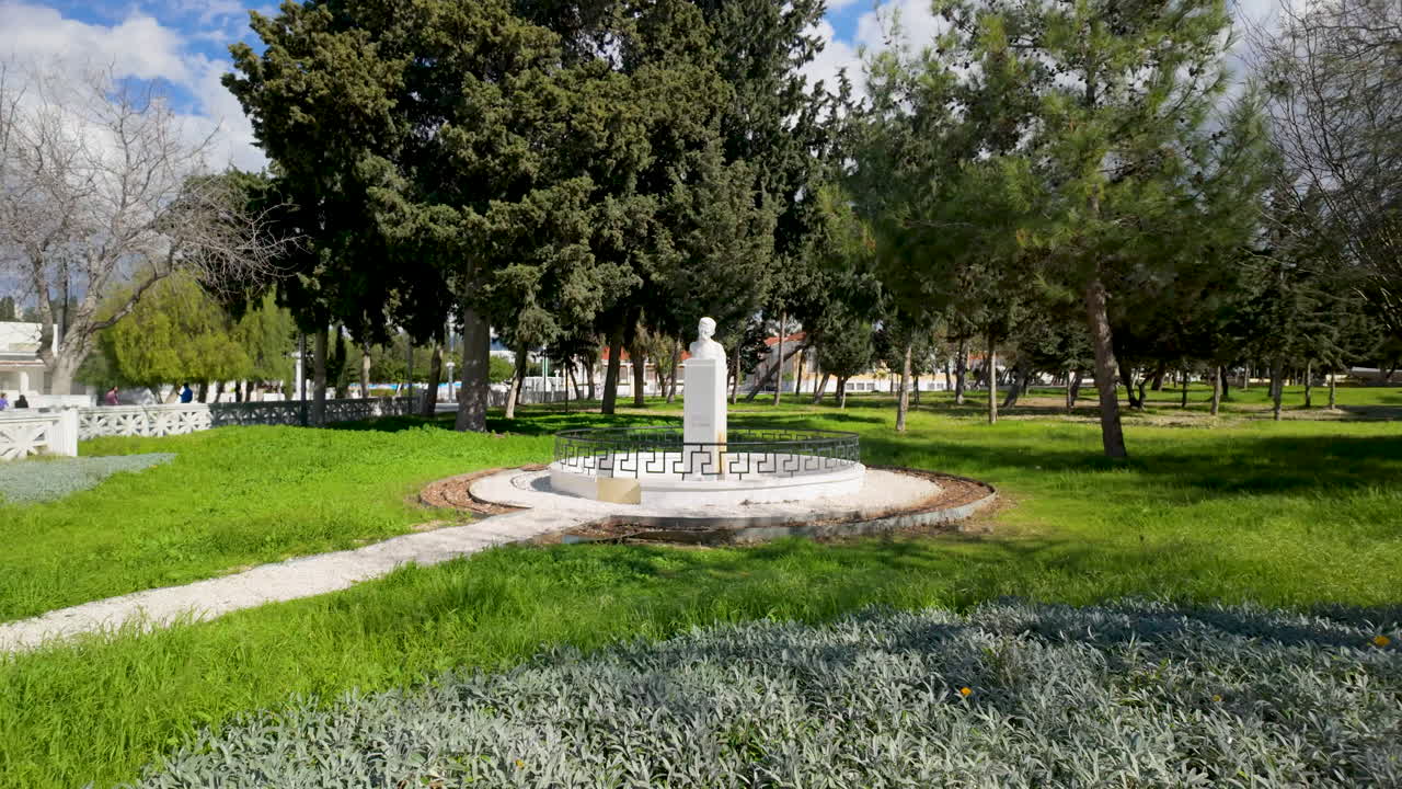 un parque público verde con una estatua blanca en un pedestal, rodeado de hierba y árboles exuberantes