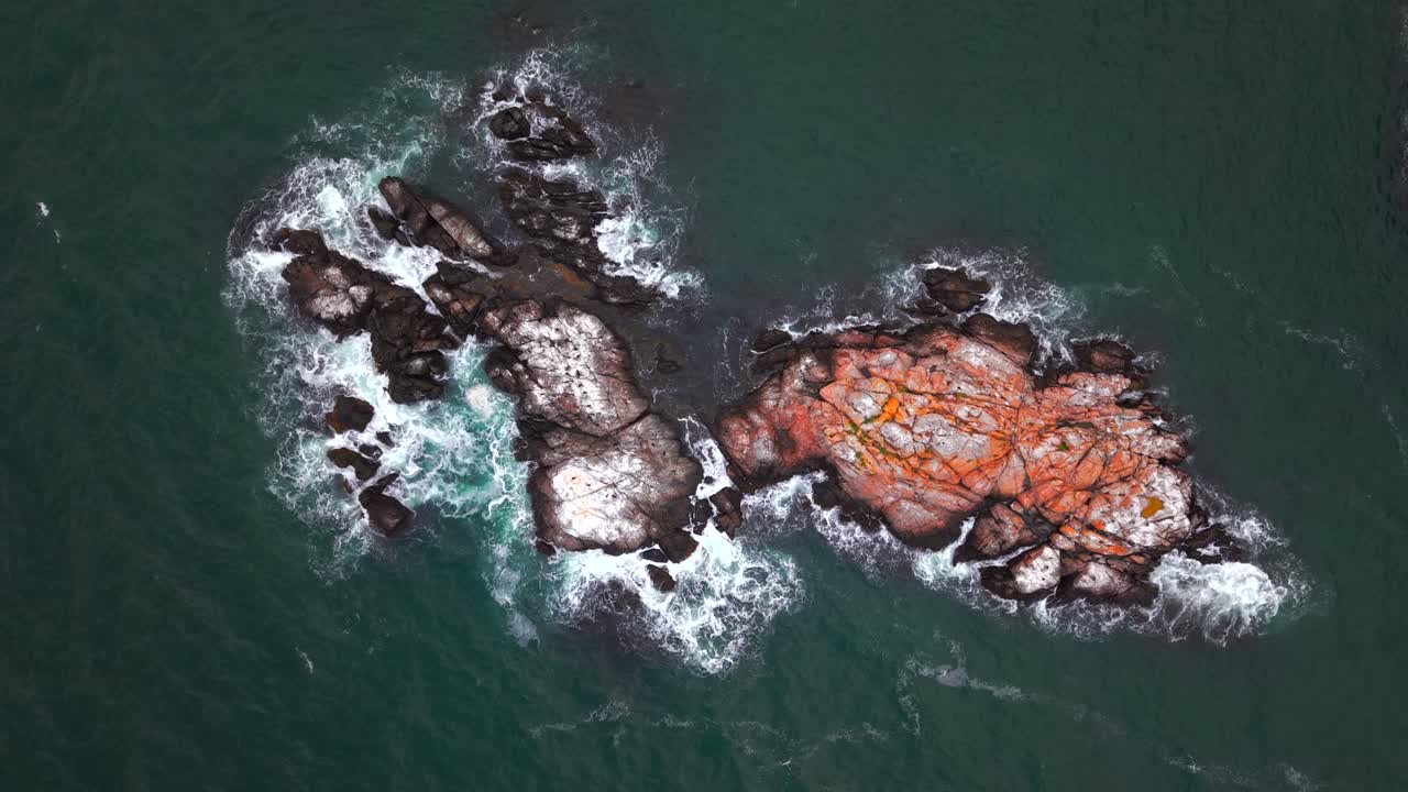 An aerial view over the rocks off the shore of Fort Wetherill State Park in Jamestown, Rhode Island on a cloudy day. The camera is tilted downward over the rocks and is stationary