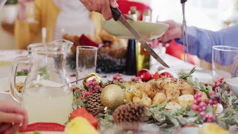 mid section of person holding fork and knife cutting chicken into pieces during christmas at home