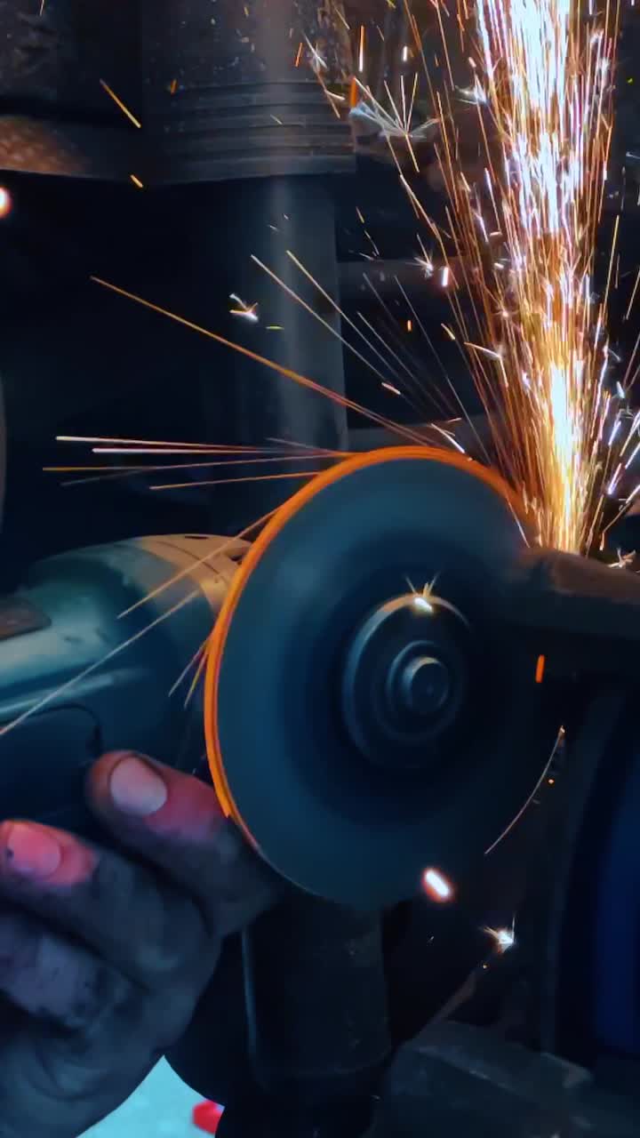 Angle grinder cutting metal with bright orange sparks. Close up of a power tool grinding metal surface creating intense circular sparks in a workshop