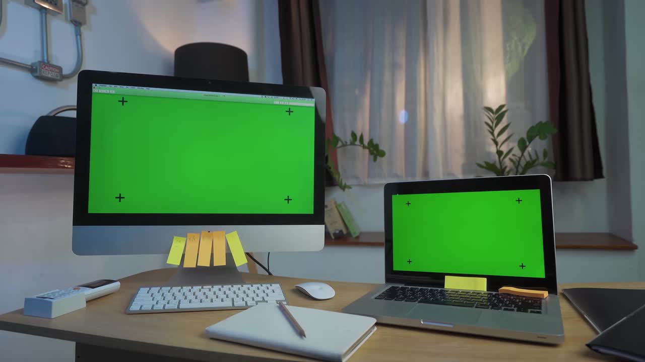 Laptop Computer and Desktop Computer Showing Green Key Screen Stands on a Desk in the Living Room Smooth Zoom out. In the Background Cozy Living Room in the Evening with Warm Lights on.