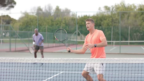 Two-diverse-male-friends-playing-doubles-returning-ball-over-net-at-outdoor-court-in-slow-motion