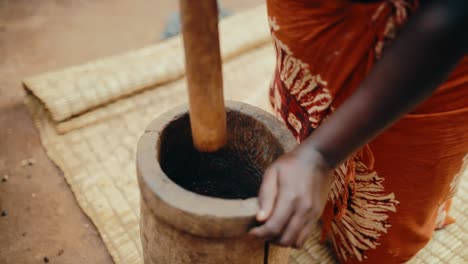 black african lady grinding coffee beans to make ground coffee using wooden mortar and pestle - traditional ugandan method