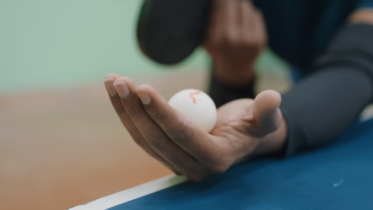 Close up of hand holding tennis ball ready for serve on indoor court, showing detail of grip, focus, and preparation before match, emphasizing precision and athletic concentration in training