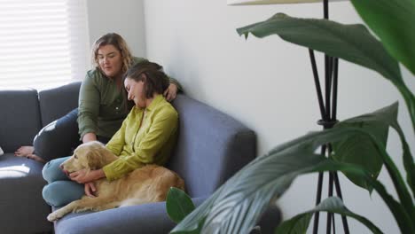 caucasian lesbian couple smiling and sitting on couch with dog