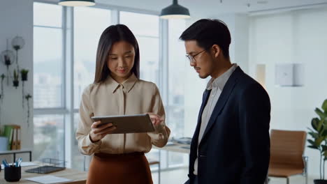 two business colleagues discussing work on a tablet in an office
