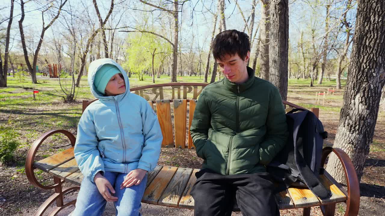 Two Young People Talking on a Bench in a Sunny Park