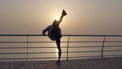 Strong-and-beautiful-woman-leans-on-the-crossbar-and-warms-up.-Throws-her-legs-across-back.-Flexibility.-Seaside.-Morning