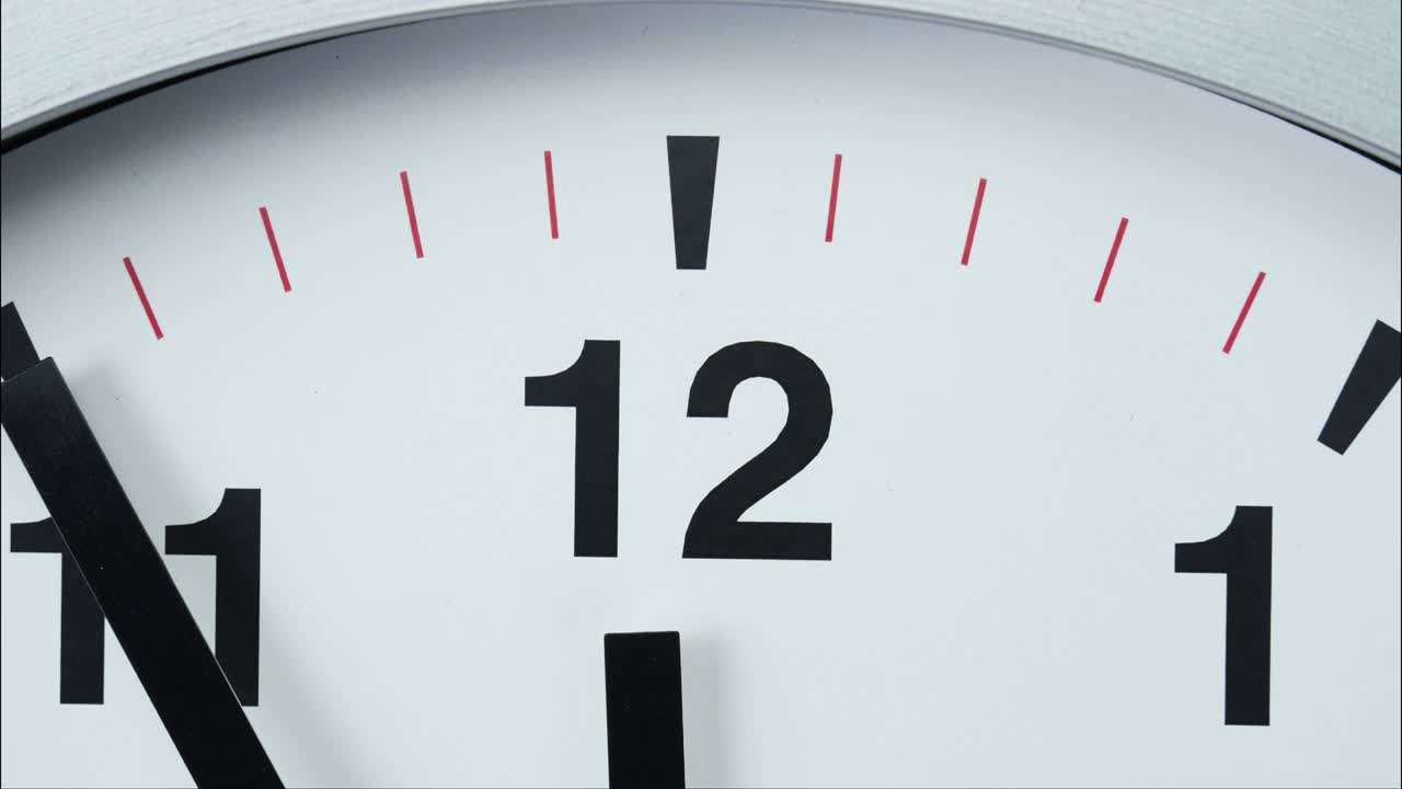 Close-up white wall clock  short hand points to the number 12.