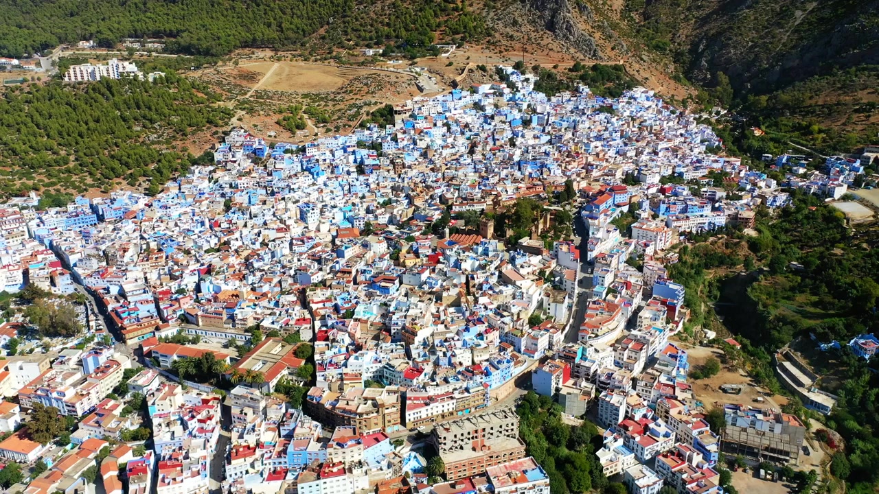 Drone luftfoto i høj højde af Chefchaouen, den blå by, omgivet af Rifbjergene i det nordlige Marokko. Levende bylandskab ideelt til rejse- og dokumentarprojekter.