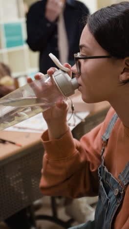 young woman drinking from a water bottle in a classroom