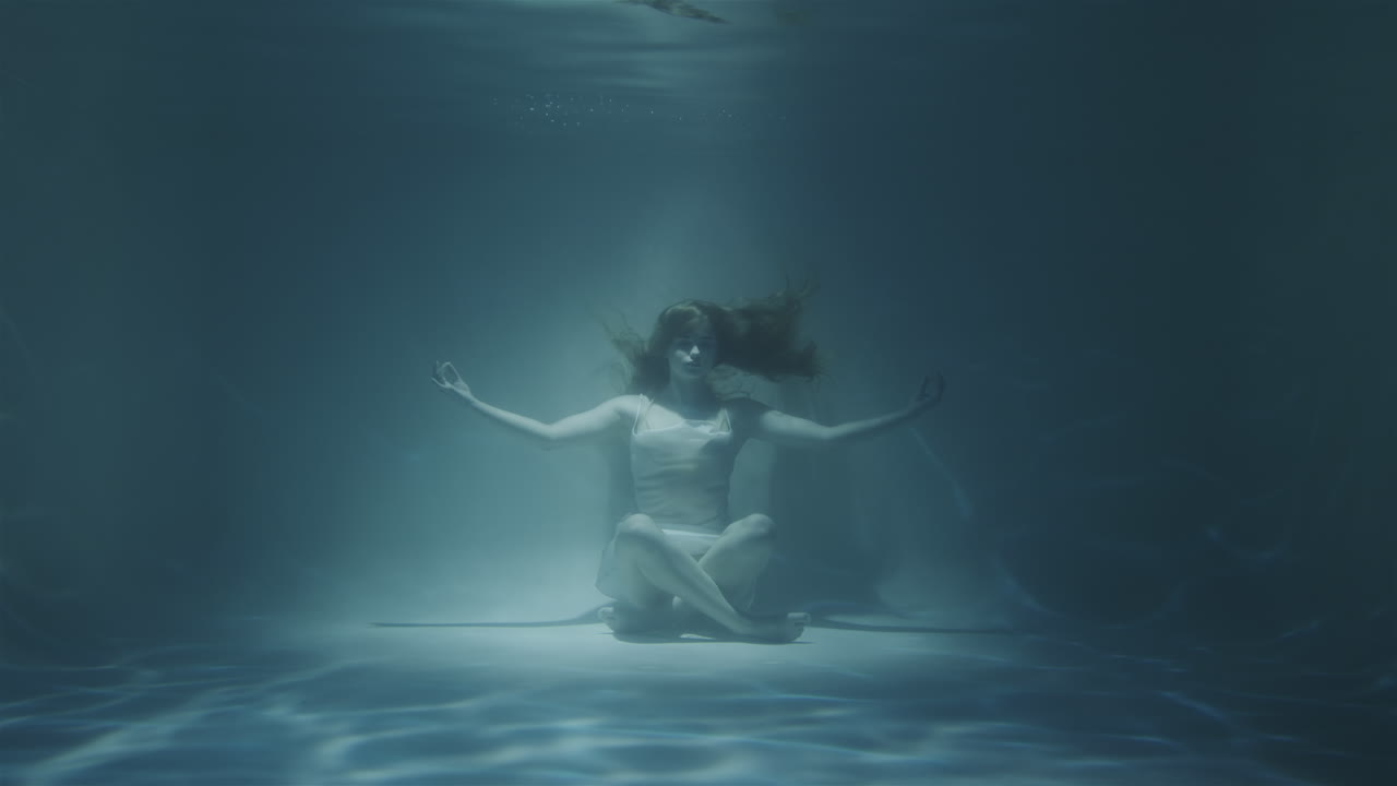 mujer pelirroja meditando bajo el agua con vestido blanco