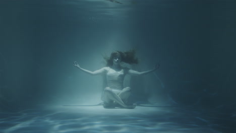 redhaired woman meditating underwater in white dress