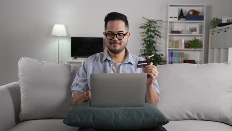 joven asiático usando una computadora portátil con tarjeta de crédito para comprar en línea y pagar en casa. cámara lenta