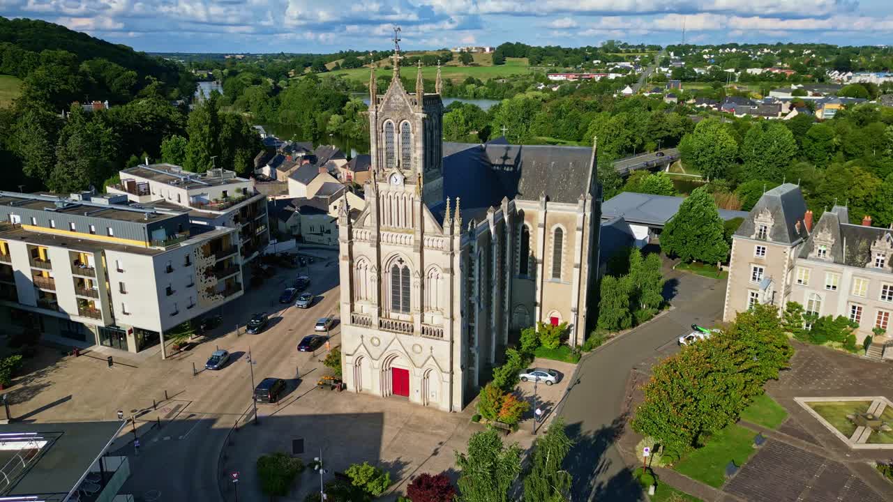 Aerial drone view of historic Saint-Pierre church in town of Changé, surrounding buildings, town square, and Mayenne river in scenic French countryside, France