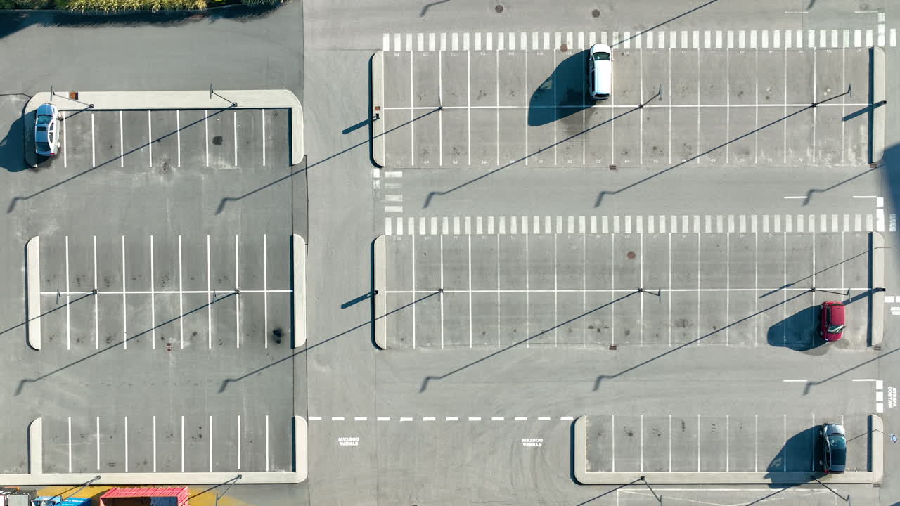 Top‑down view of nearly empty parking lot with light pole shadows and marked parking rows in sunlight