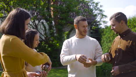 caucasian young man teaching his friends how to hold petanque balls to start the game