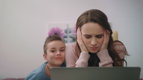 Busy-mom-embrace-son-while-working-on-laptop-computer-at-home