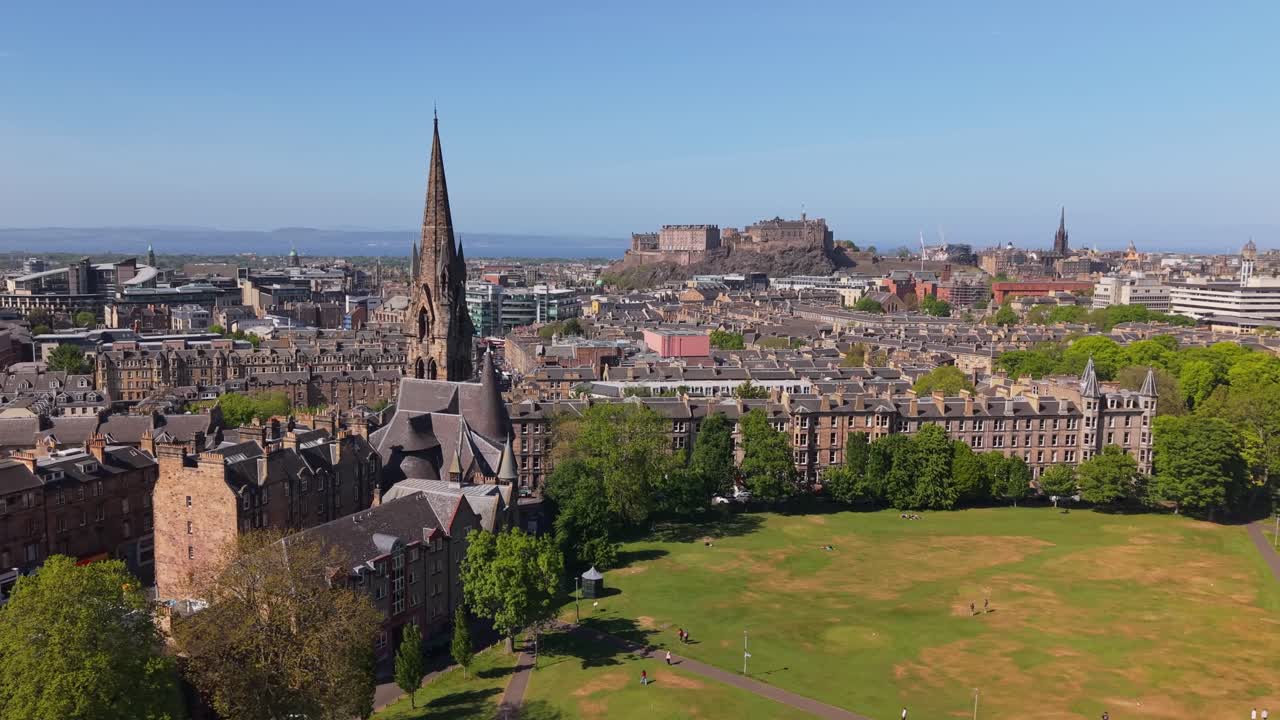 Drone orbits the Barclay Viewforth Church in Edinburgh, revealing the lush Meadows park and Edinburgh Castle rising majestically in the distance
