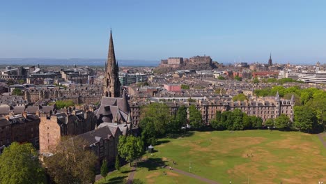 drone orbits the barclay viewforth church in edinburgh, revealing the lush meadows park and edinburgh castle rising majestically in the distance